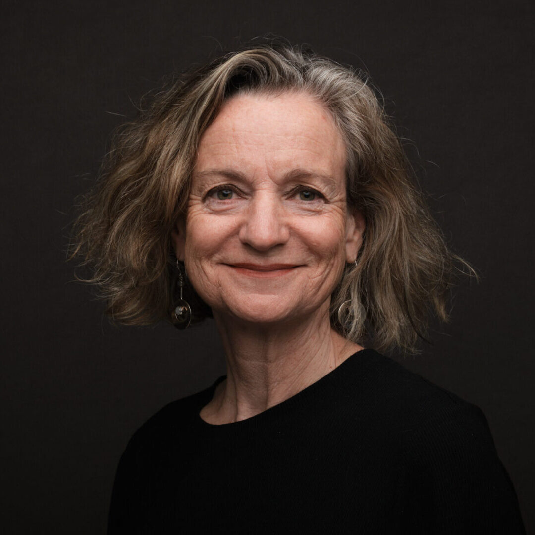Smiling woman with short wavy hair against a dark background.