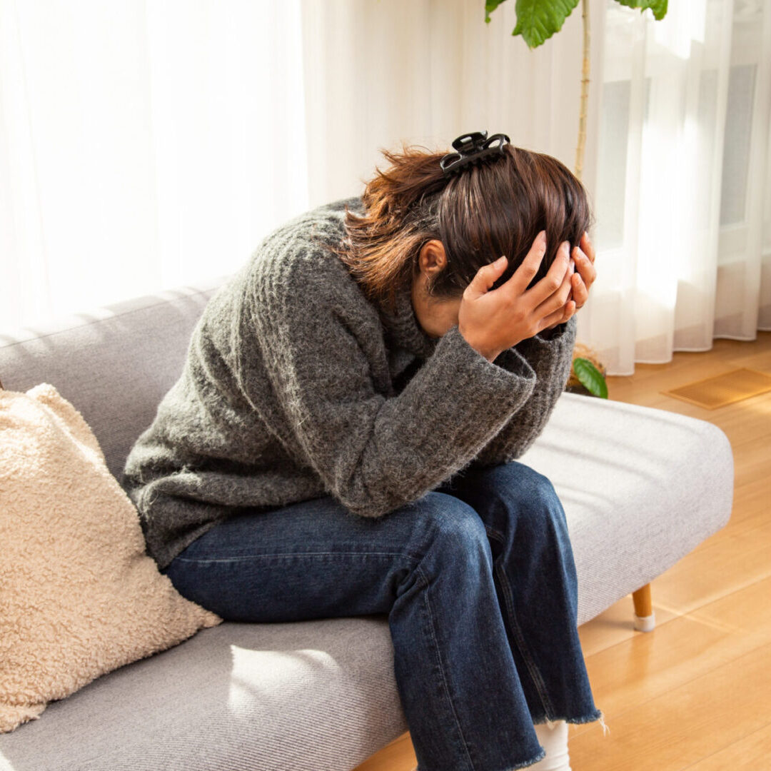 Woman sitting on couch holding her head, appearing stressed or upset.
